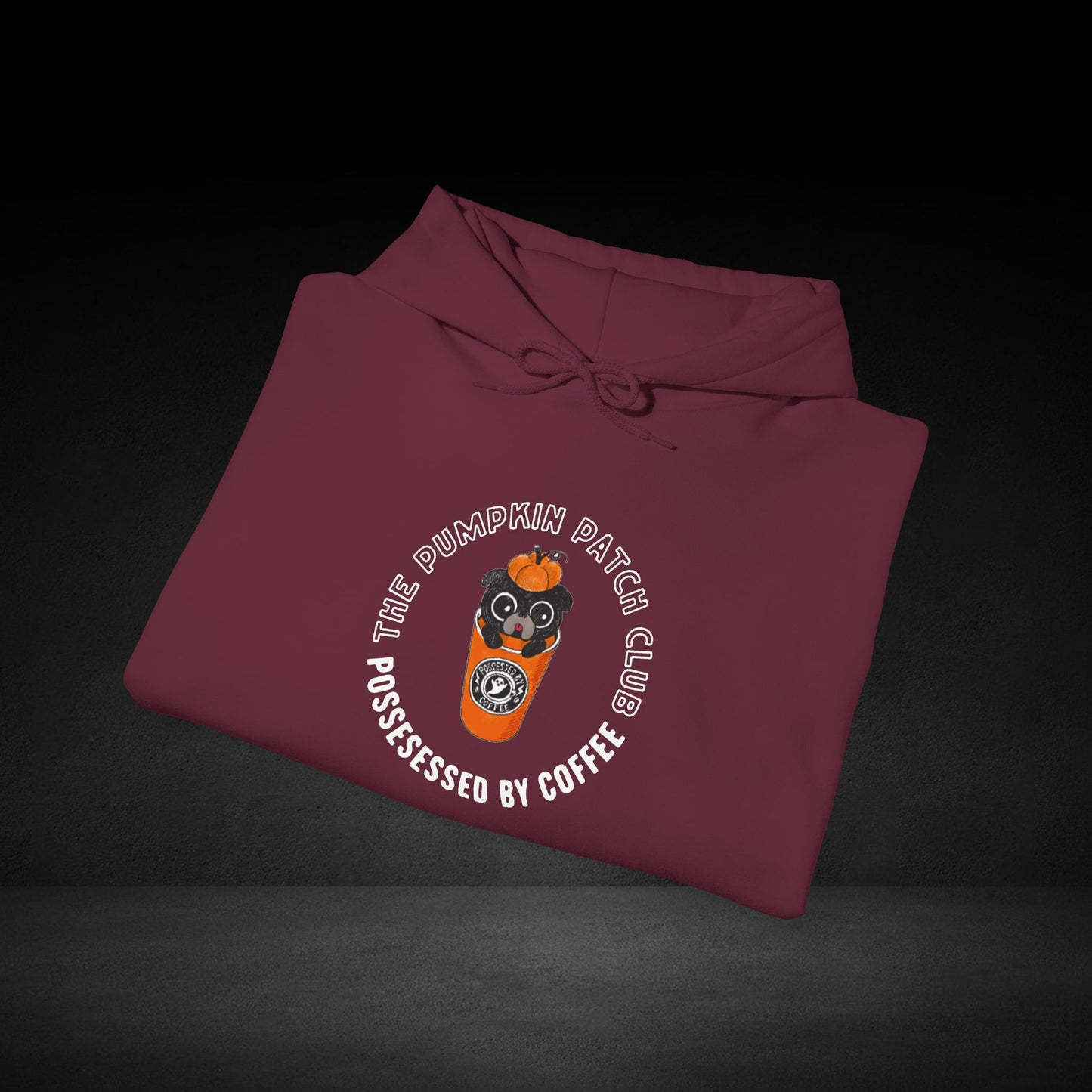 A maroon hoodie with a graphic design and text on it, laid out on a dark background.